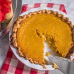 Depicts flakiest pie crust originally by Bon Appetit filled with James Beard's pumpkin pie. Pie plate is white and is set on marble table with red buffalo plaid napkin
