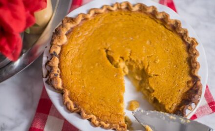 Depicts flakiest pie crust originally by Bon Appetit filled with James Beard's pumpkin pie. Pie plate is white and is set on marble table with red buffalo plaid napkin