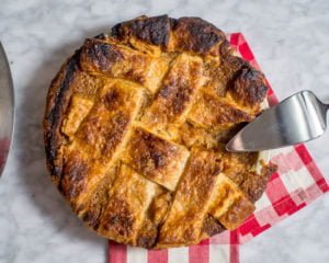 Overhead view of lattice weave with foolproof vodka pie crust and a sweet potato pie filling. It is set on a marble table and a red buffalo plaid napkin and a pie server