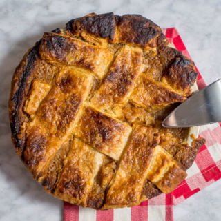 Overhead view of lattice weave with foolproof vodka pie crust and a sweet potato pie filling. It is set on a marble table and a red buffalo plaid napkin and a pie server