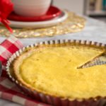 Close-up photo of no-shrink pie crust originally by Milk Street. Also shows custard brown sugar tart filling with a red buffalo plaid napkin and flowers